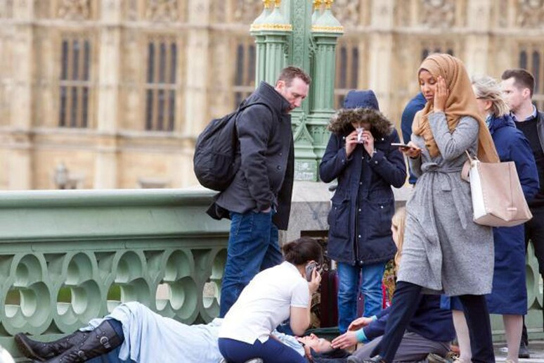 Nella foto una donna con il capo coperto da un velo passa accanto ad  una delle vittime dell 'attacco terroristico del 22 marzo a Londra. L 'immagine era stata usata dai profili social anti-islamici per sostenere teorie xenofobe, senza spiegarne il contesto - RIPRODUZIONE RISERVATA