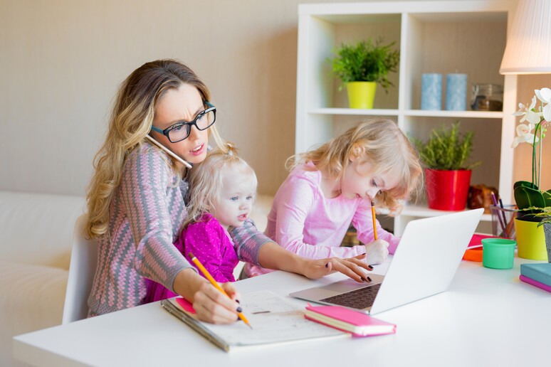 Una donna al computer e intanto aiuta i figli nei compiti . foto iStock. - RIPRODUZIONE RISERVATA